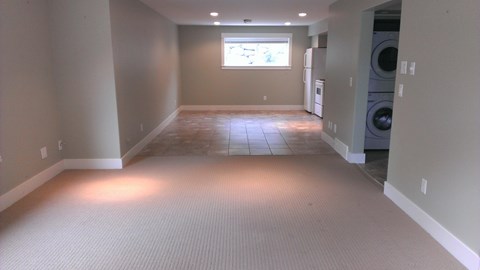 A large empty room with a window and a washer and dryer in the corner.